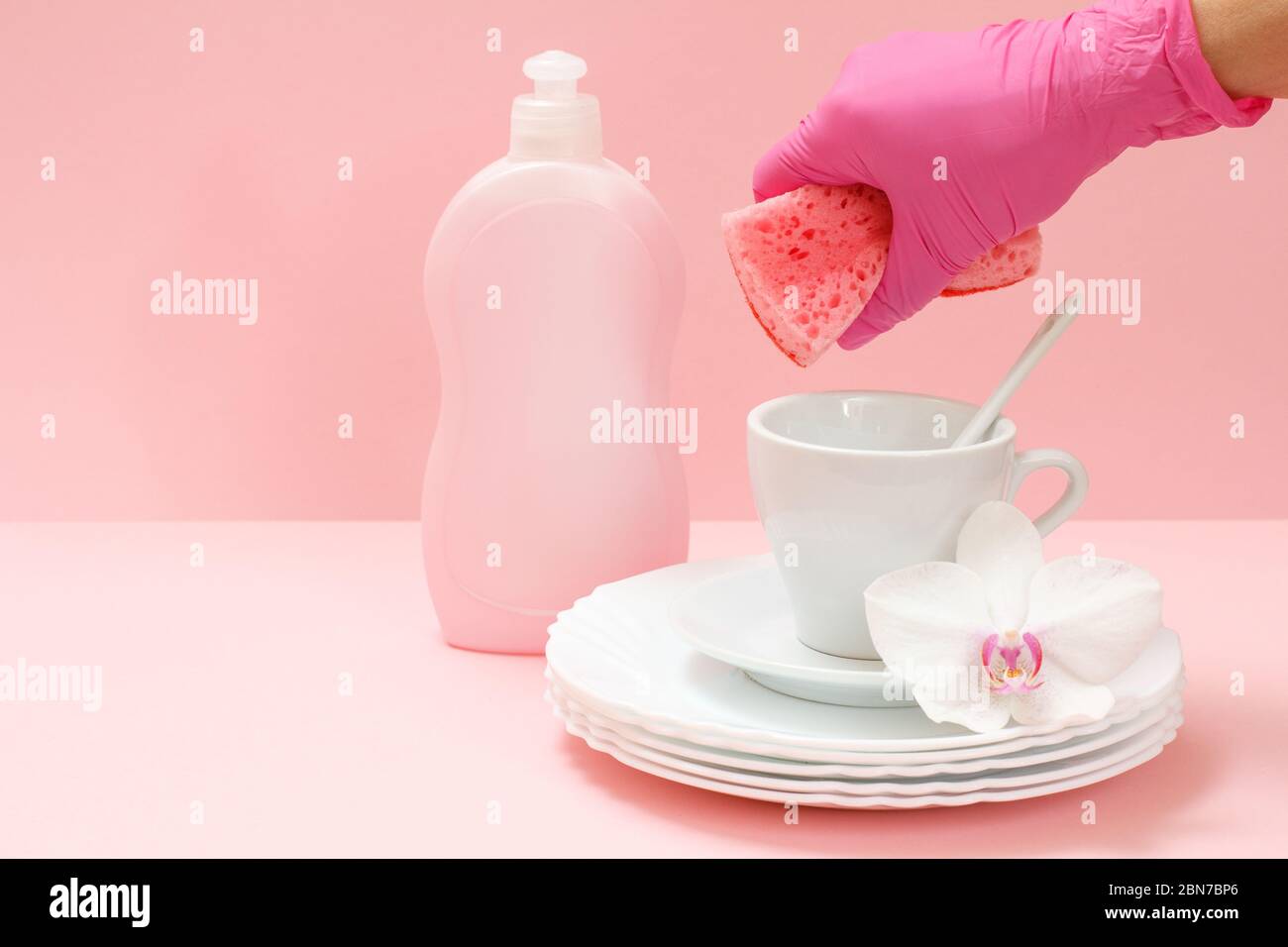 Woman's hand in a rubber protective glove with a sponge, white plates ...