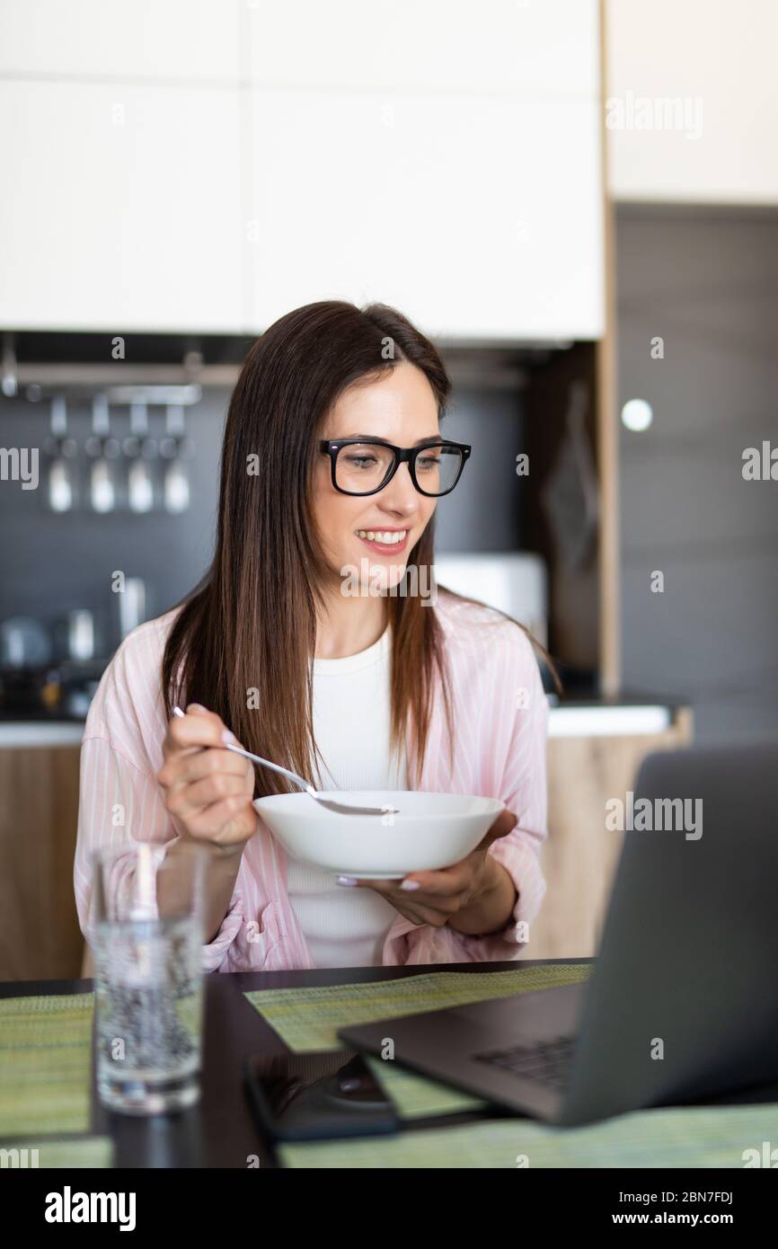 Young woman using on laptop computer and eating breakfast in the kitchen Stock Photo