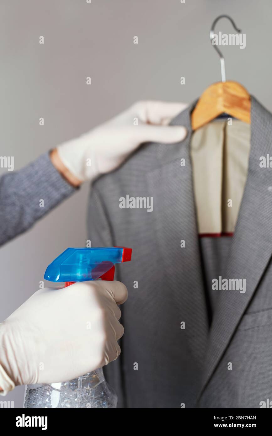 closeup of a man, wearing latex gloves, disinfecting a sport jacket hanging  on a clothes hanger by spraying a disinfectant from a bottle Stock Photo -  Alamy