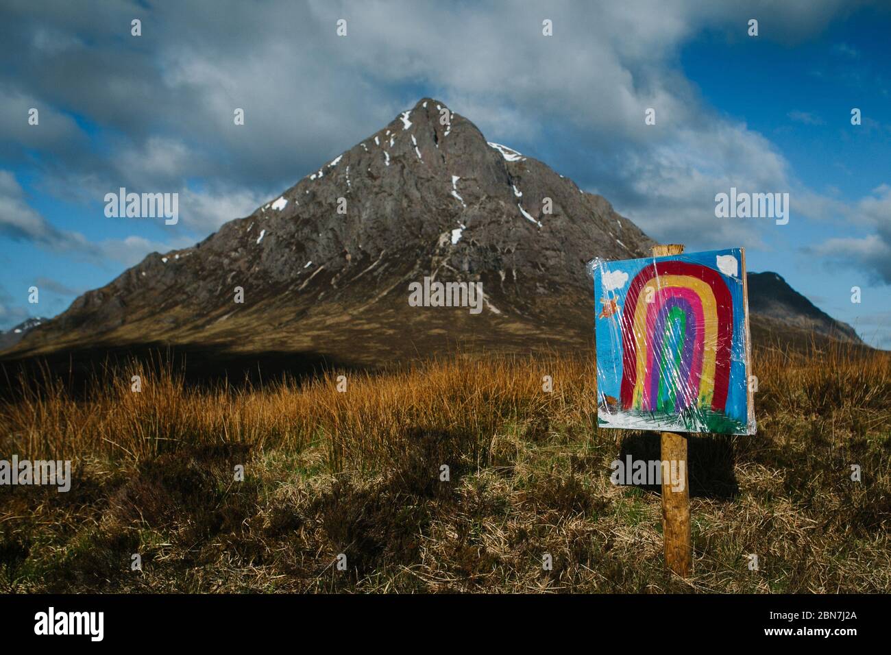 A rainbow painted on a sign by a child, in front of the Buachaille Etive Mor, in Glencoe, Scotland, during the Corona Virus pandemic lockdown. Stock Photo