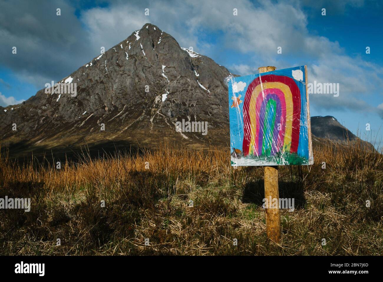 A rainbow painted on a sign by a child, in front of the Buachaille Etive Mor, in Glencoe, Scotland, during the Corona Virus pandemic lockdown. Stock Photo