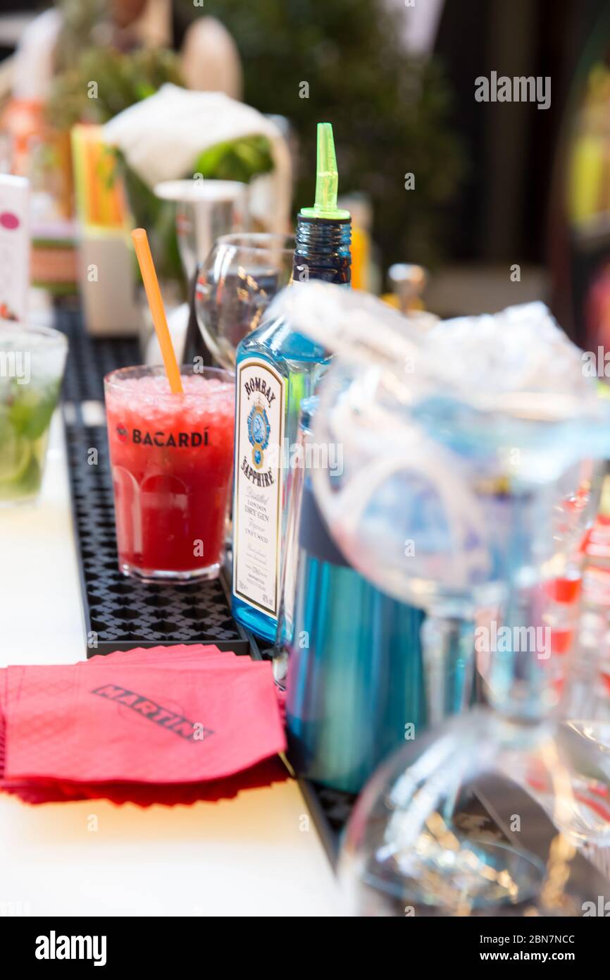 Red Cocktail Served on Open Bar with Alcohol Bottle of Bombay Sapphire with Pouring Stopper Stock Photo