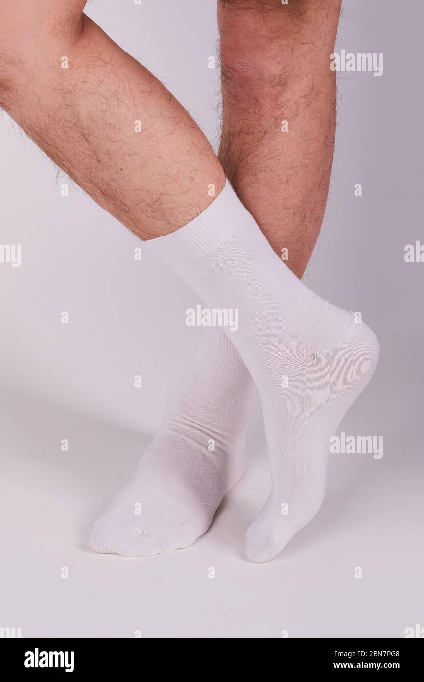 Man wearing new white cotton blank socks on a white background. Detailed closeup studio shot. Male legs wearing socks Stock Photo
