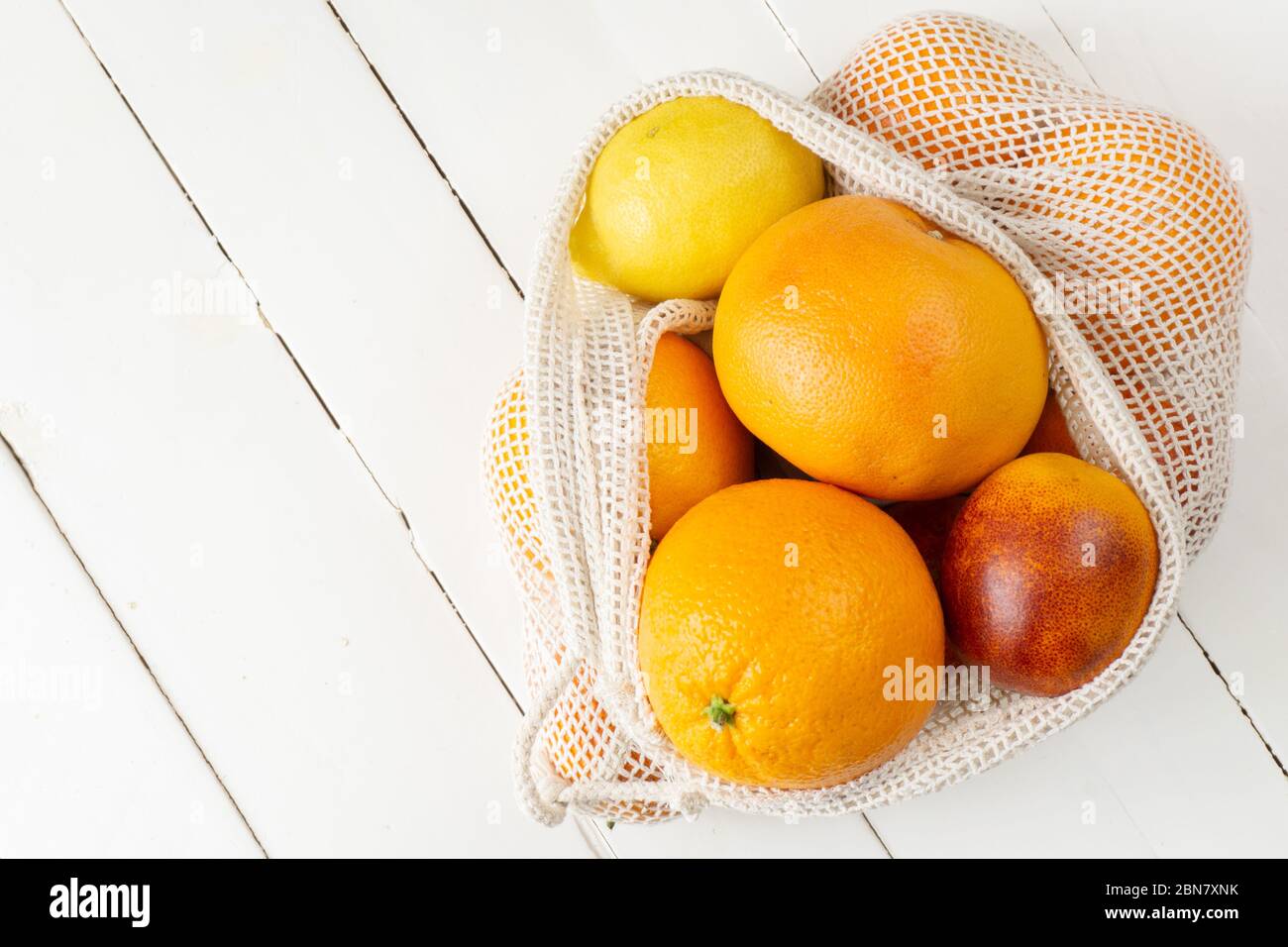 Orange, lemon and grapefruit in eco bag on white wooden background. Citrus fruit. Zero waste, eco friendly or plastic free lifestyle concept. Copy space, vertical. Stock Photo