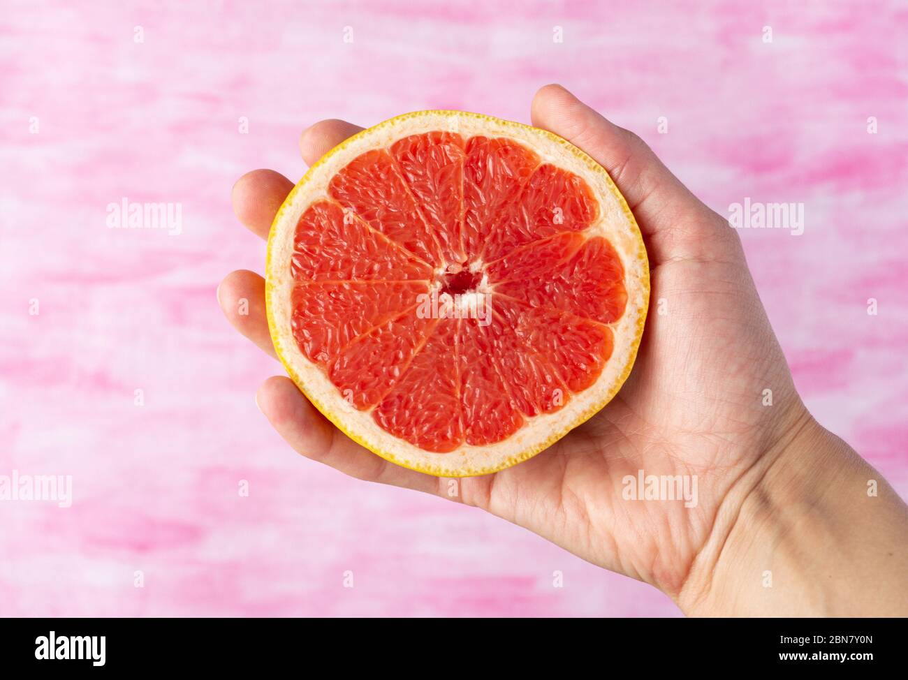 Hand holds half of grapefruit on pink background. Close up, top view.  Stock Photo