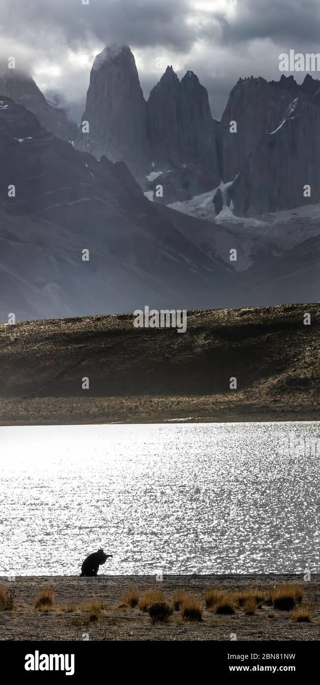 A lone photographer in front of Laguna amarga with the Cordillera Paine mountain range in the background with the three Torres del Paine. Stock Photo