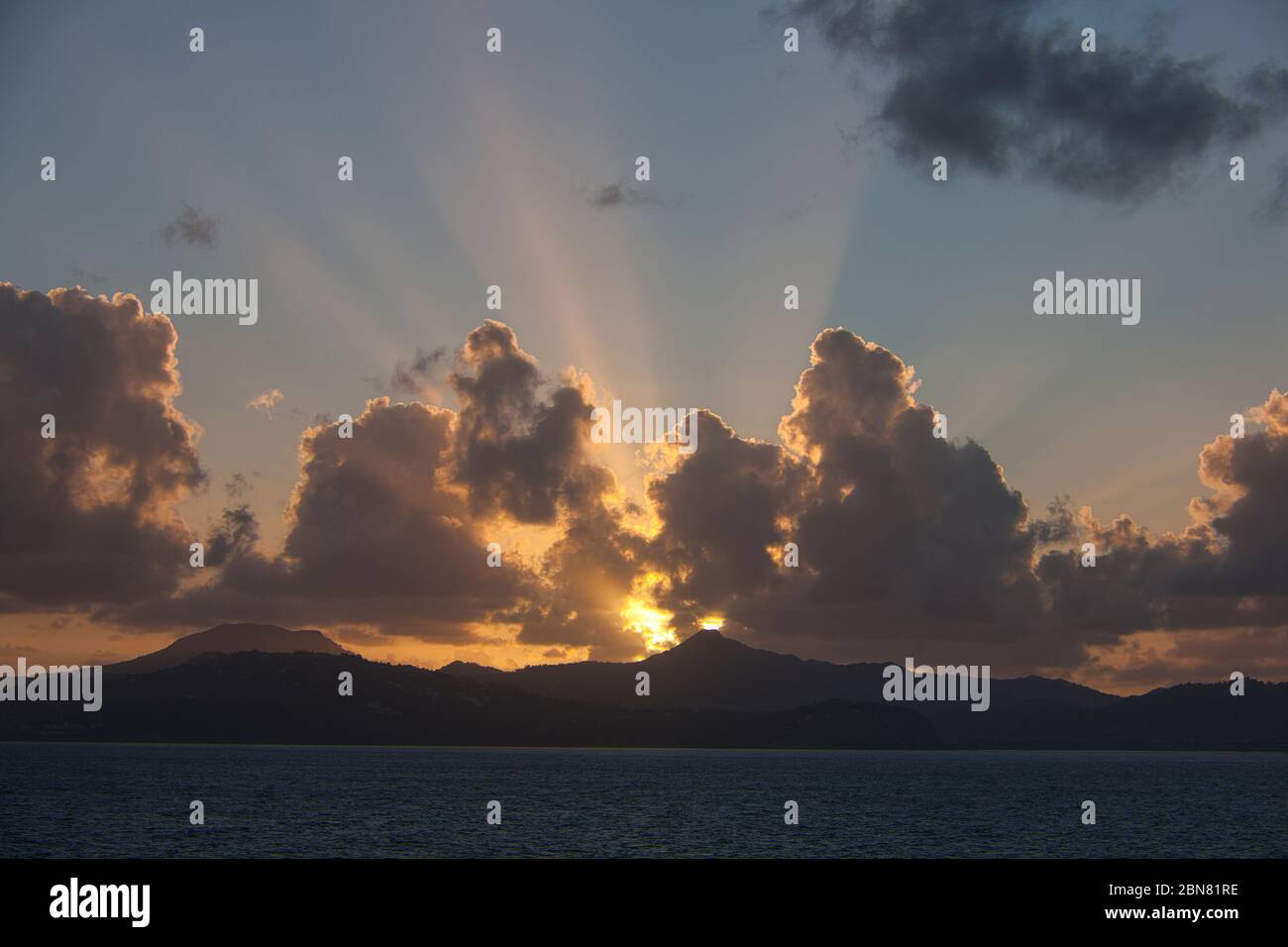 Spectacular sunrise over the hills of the west coast of St Lucia in the Caribbean, West Indies. Clouds and sun rays in the blue sky Stock Photo