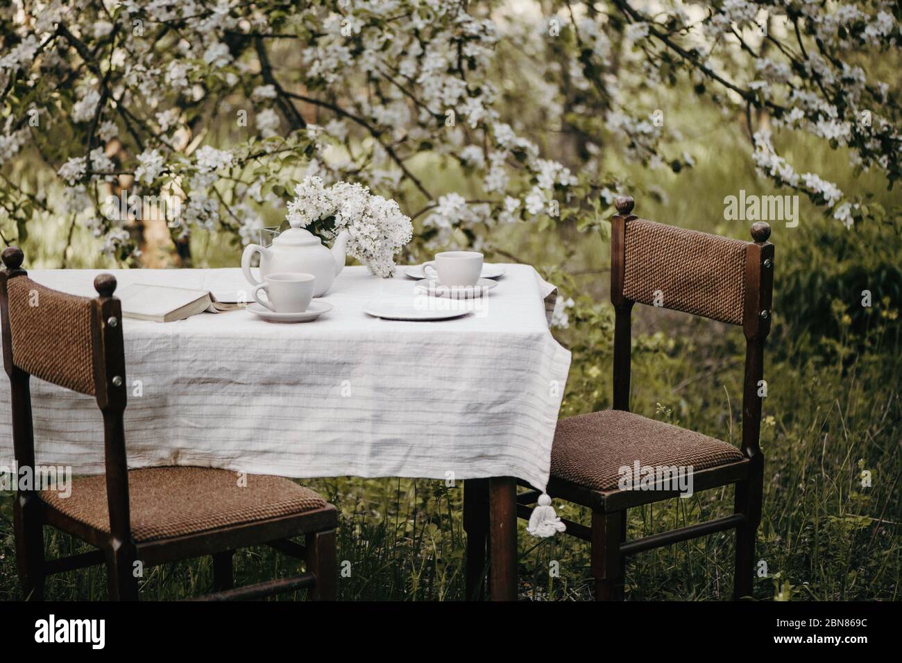 Dinner table with tea cups and tea pot at beautiful blooming garden. Stock Photo