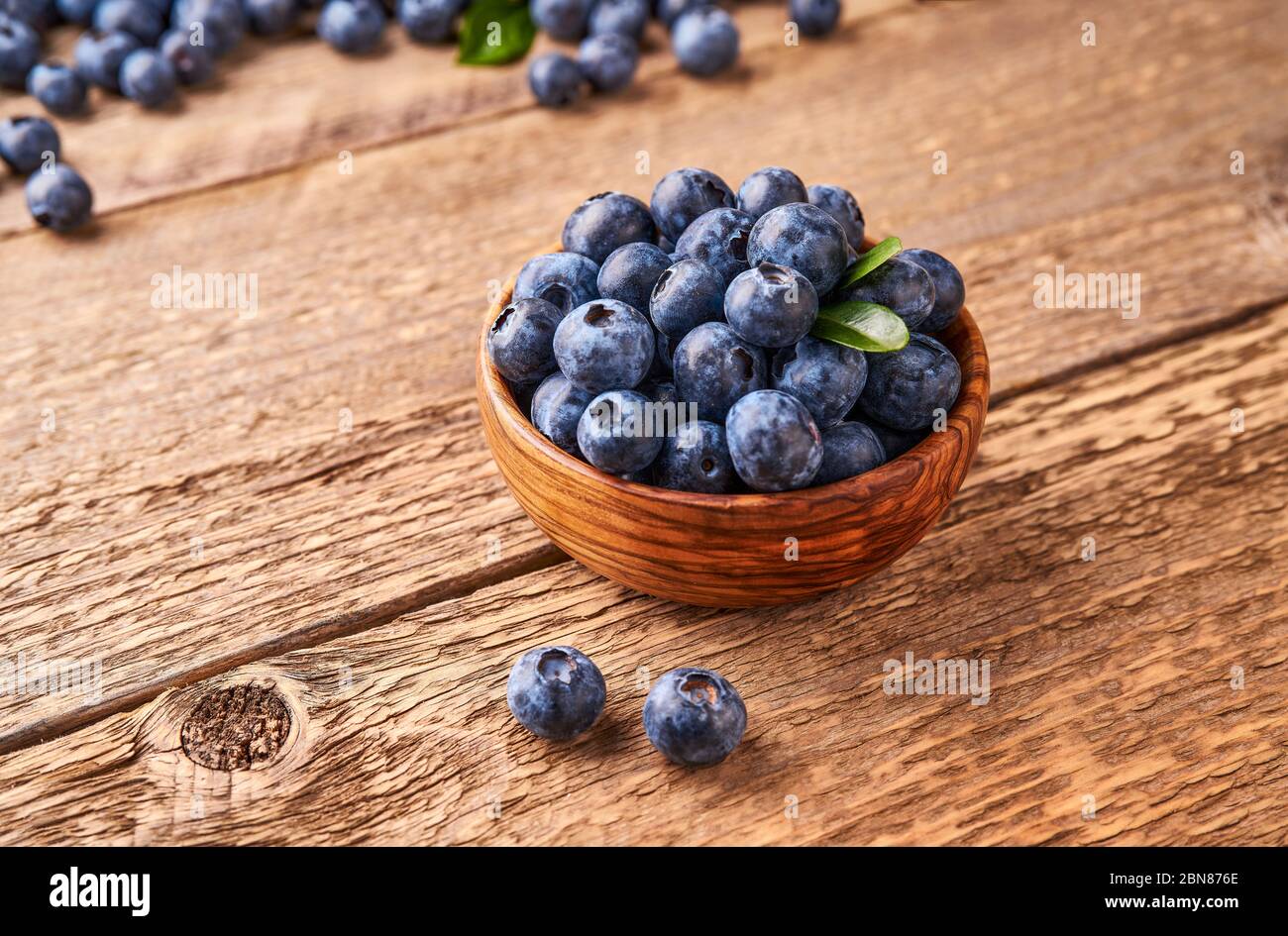 Fresh blueberries with blueberry leaves in wooden bowl on wooden background. Stock Photo