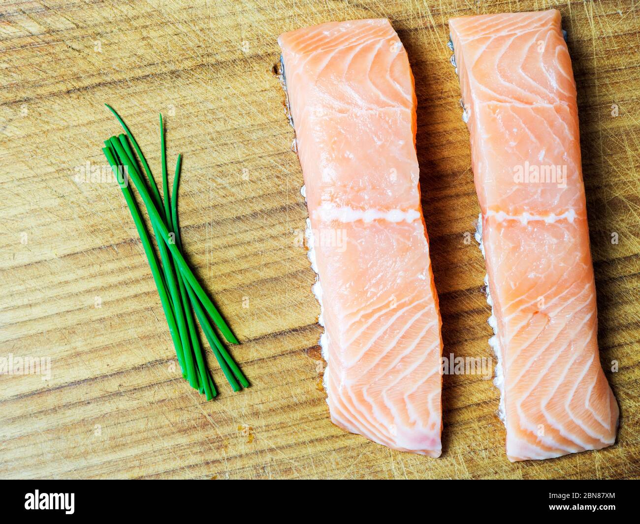 Two raw salmon fillets on a wooden chopping board with fresh chives ...