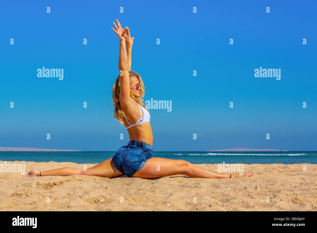 Young blonde dutch woman  practices yoga on beach Stock Photo