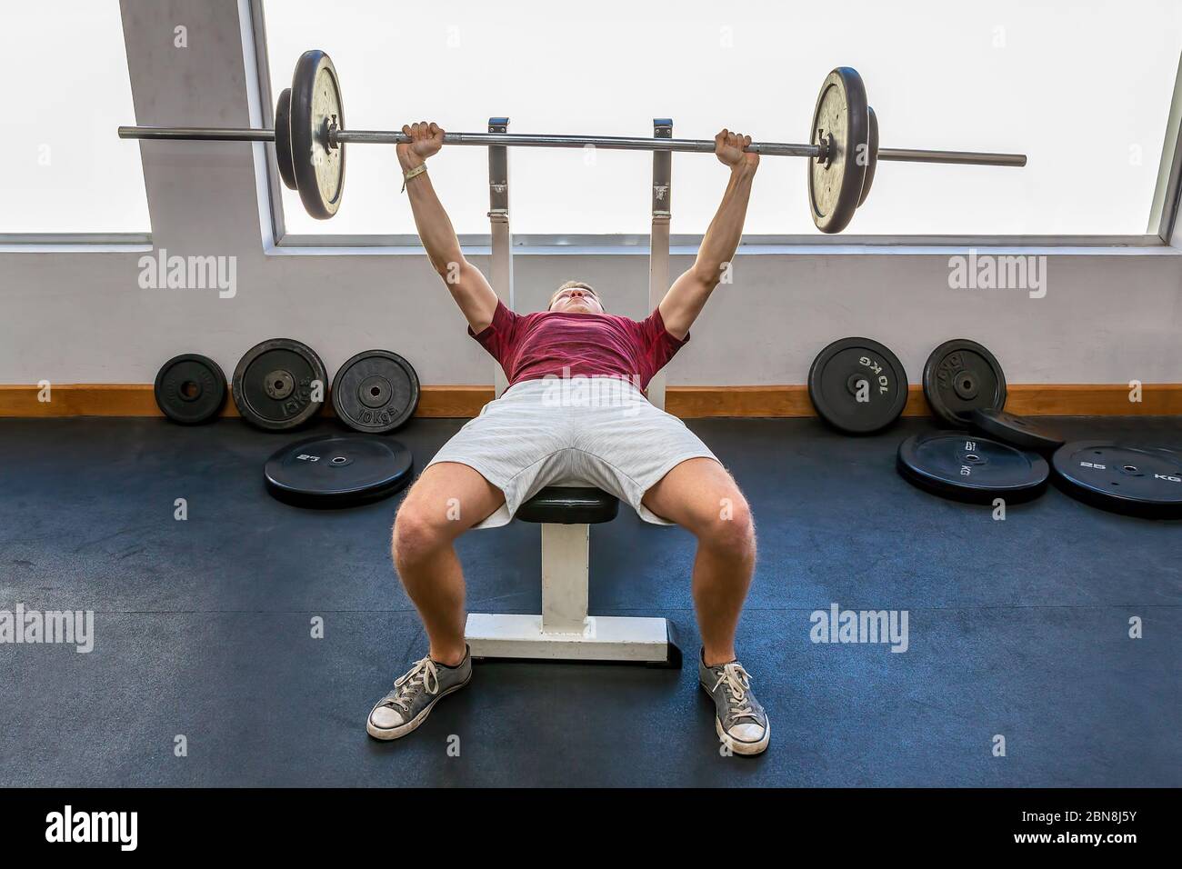 Young european man bench press with barbell in fitness room Stock Photo