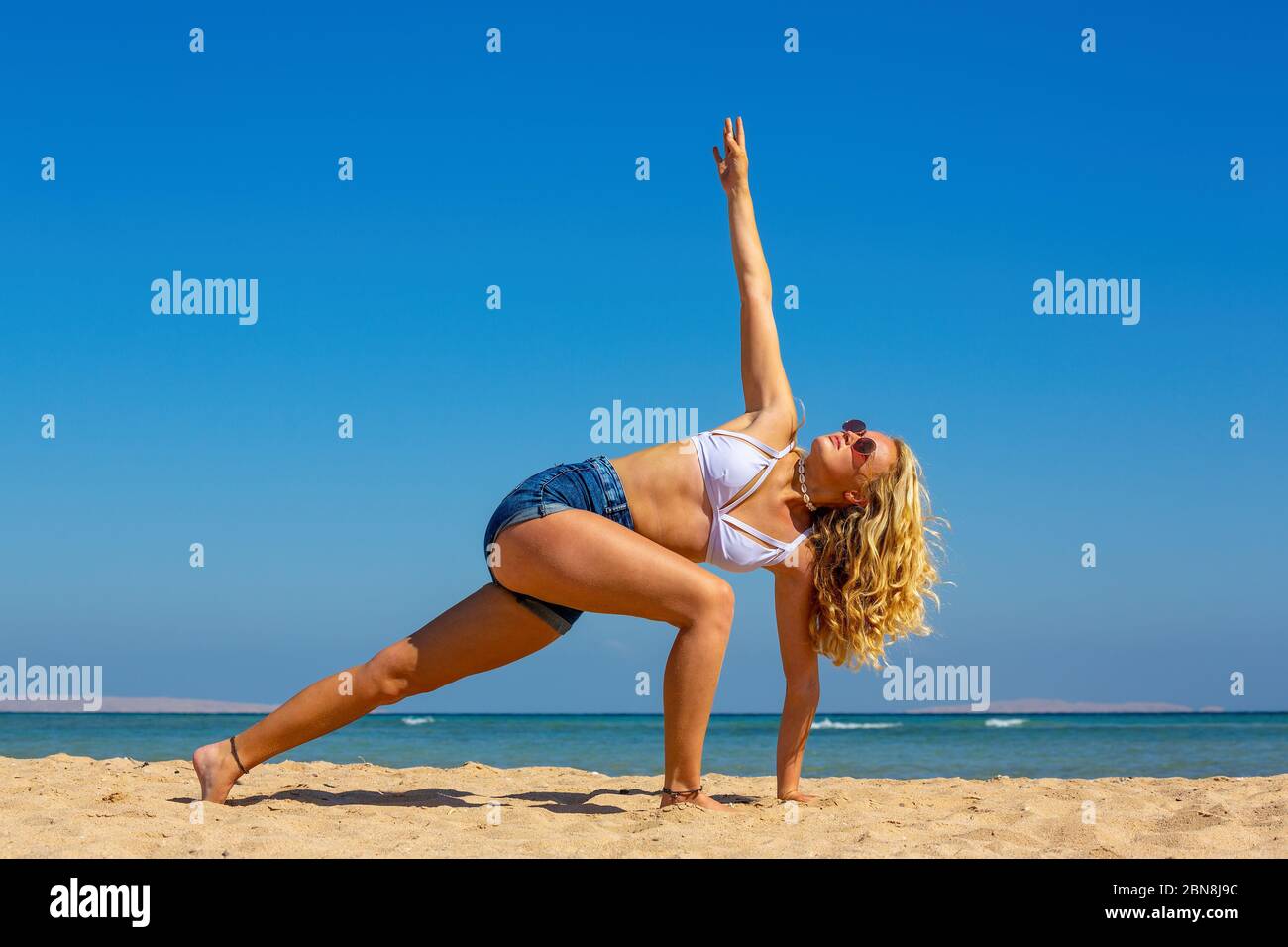 Young blonde dutch woman training yoga pose on beach near sea Stock Photo