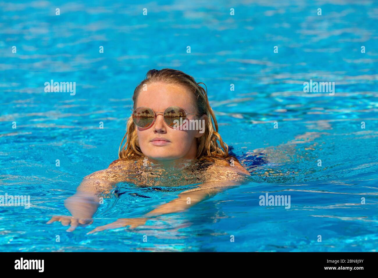 Young caucasian woman swims in blue water of outdoor swimming pool Stock Photo