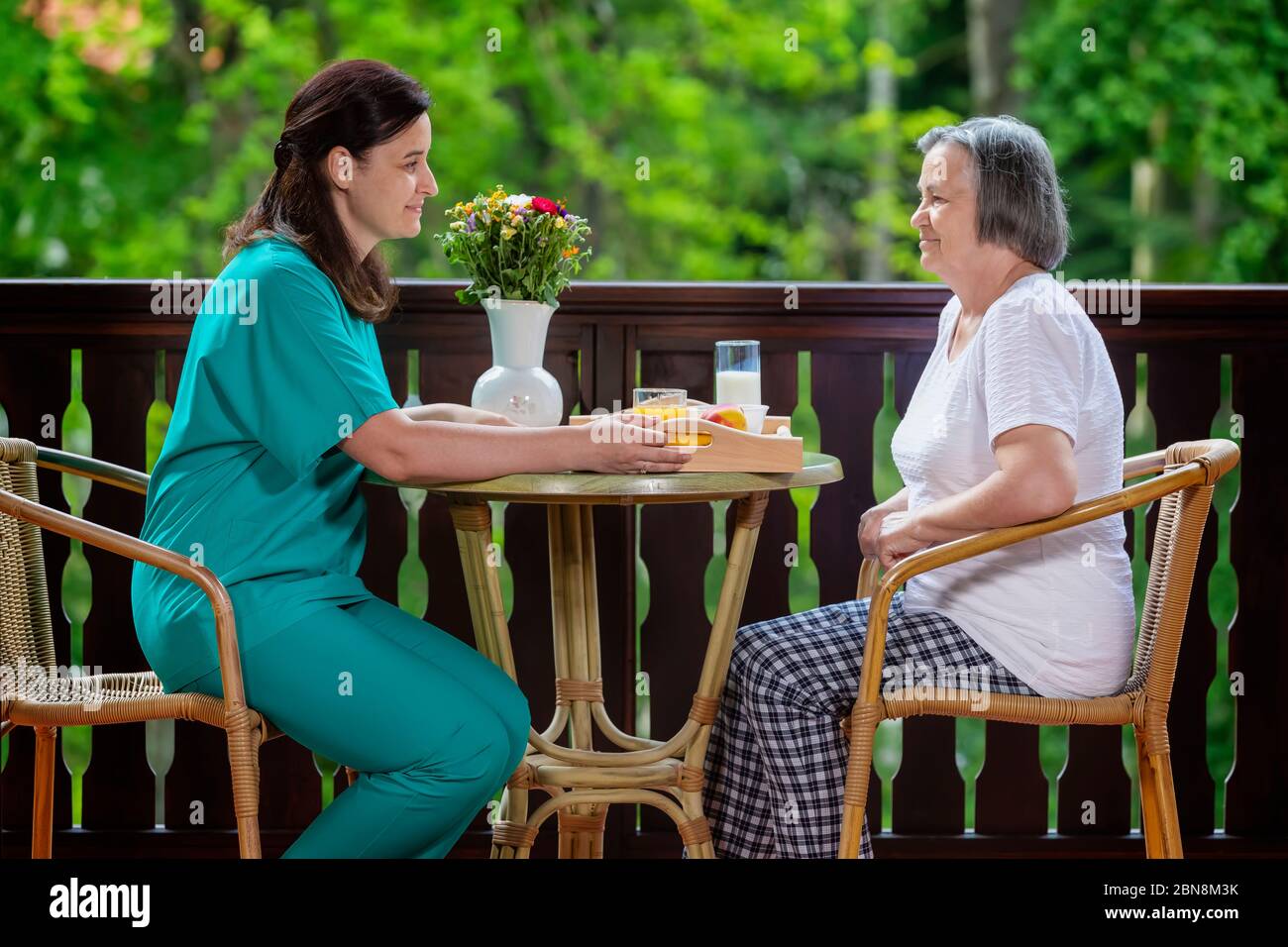 Smiling young carer serving breakfast to happy senior woman at nursing home Stock Photo