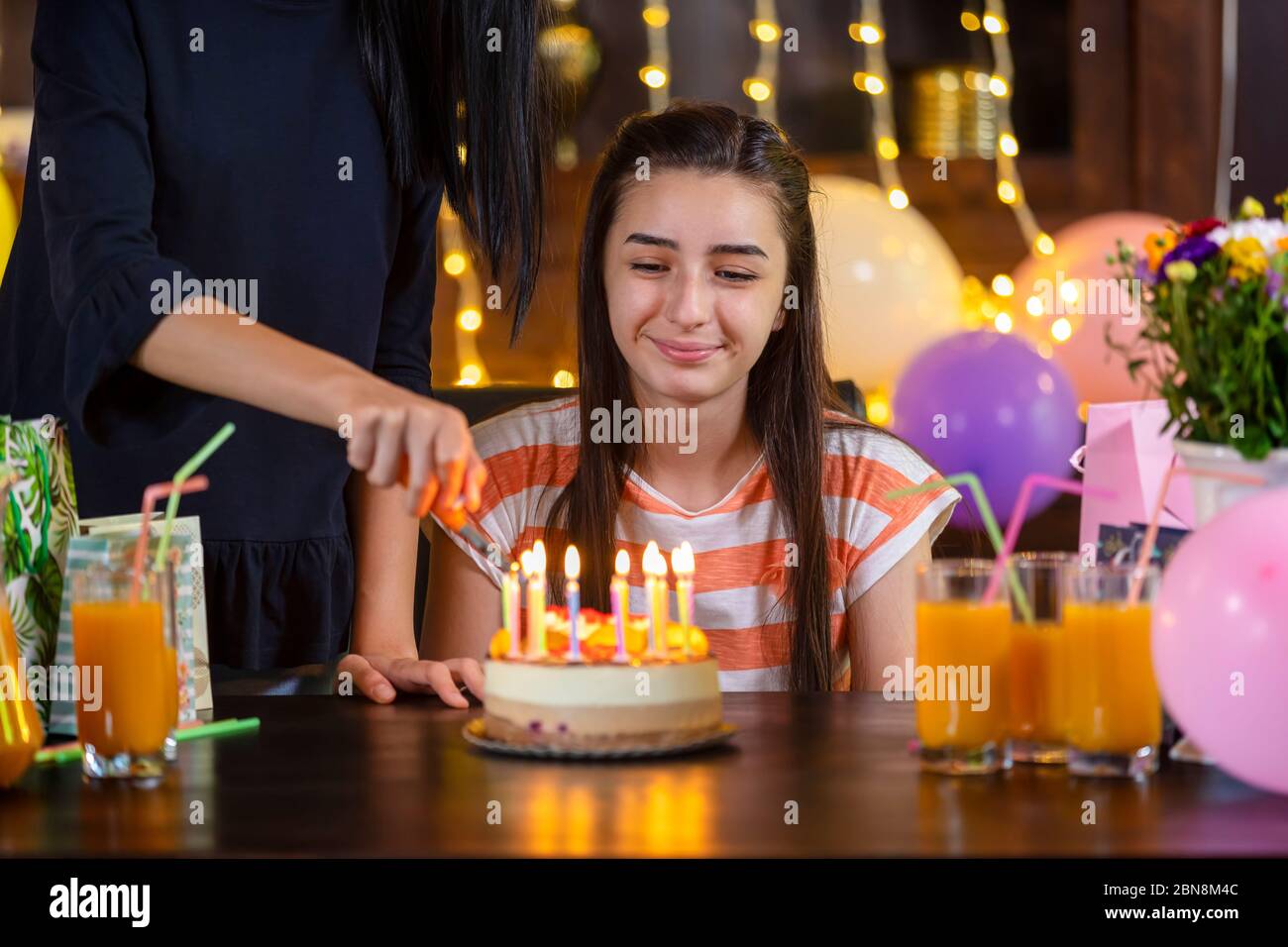 Happy teen girl and mother with birthday cake at anniversary party. Lighting candles on birthday cake. Stock Photo