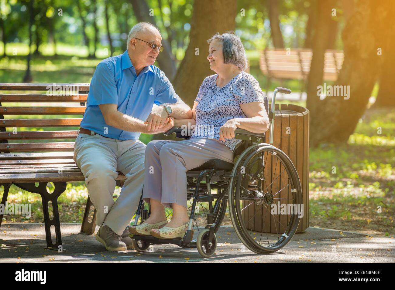 Senior man talking with woman in wheelchair outside in summer park. Stock Photo