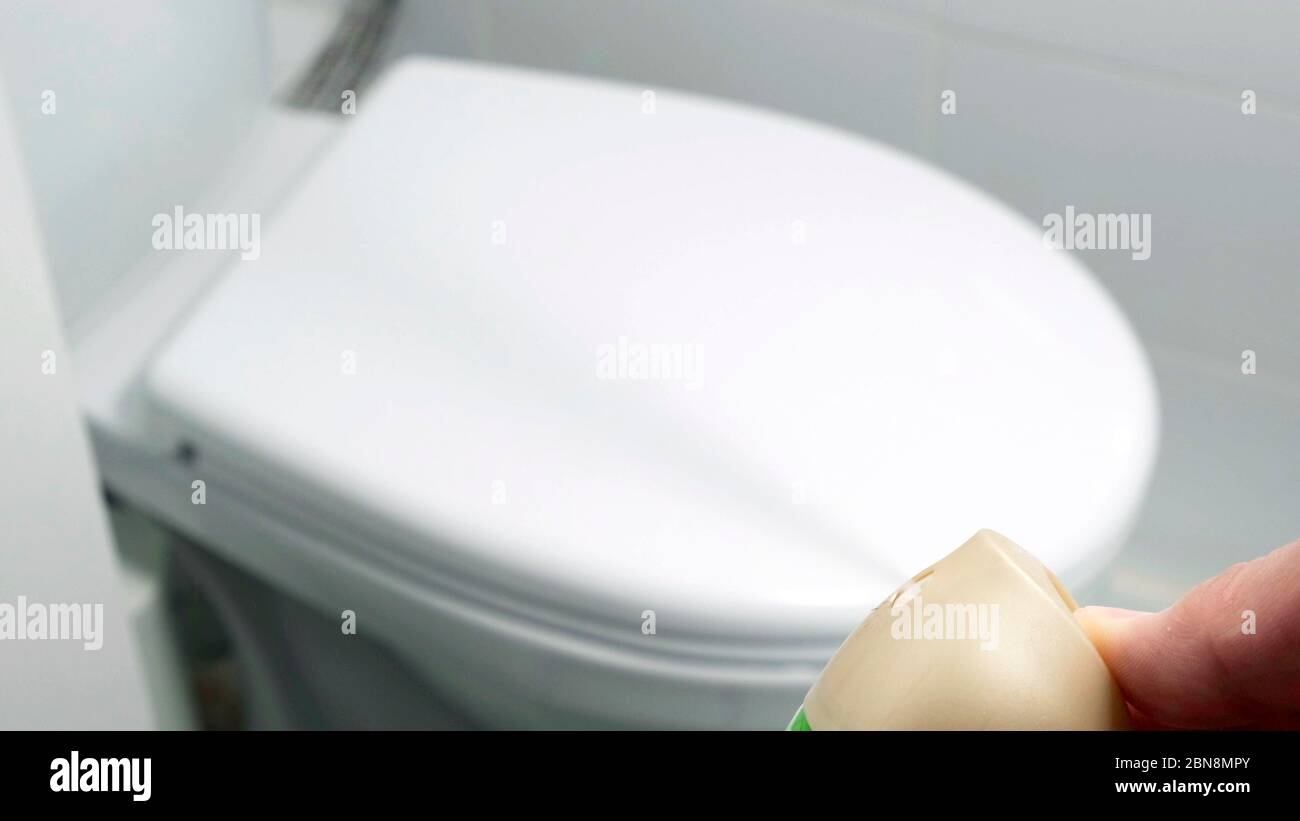 Air freshener being sprayed inside white toilet. Stock Photo