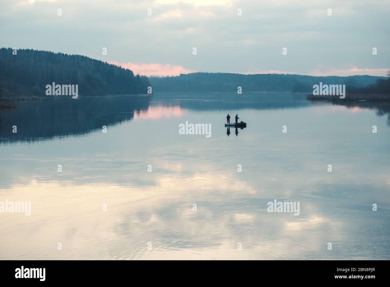 Silhouettes of fishermen in a boat on a lake surface. Stock Photo