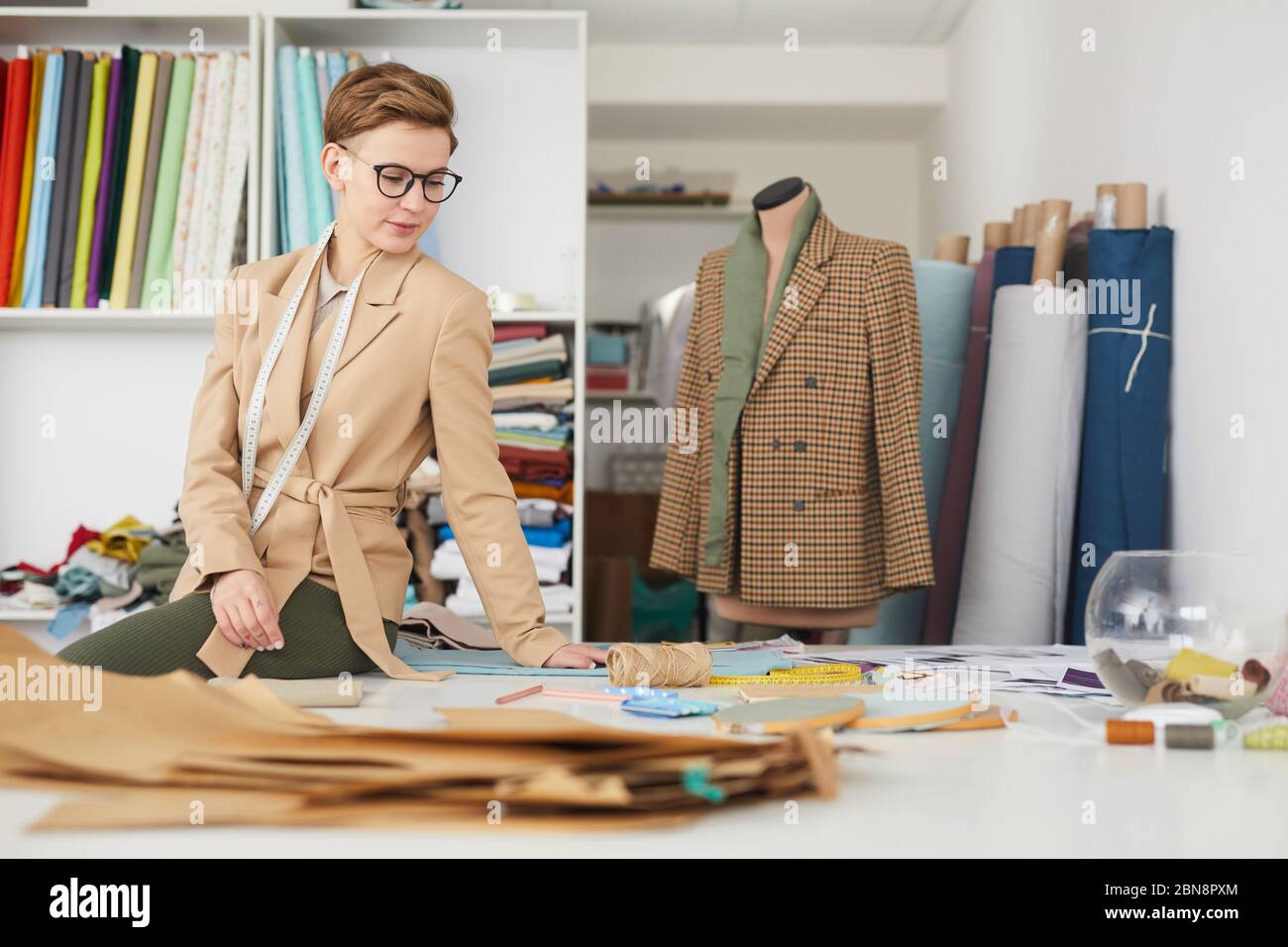 Young tailor working at her workplace with patterns she is going to make a new jacket in workshop Stock Photo