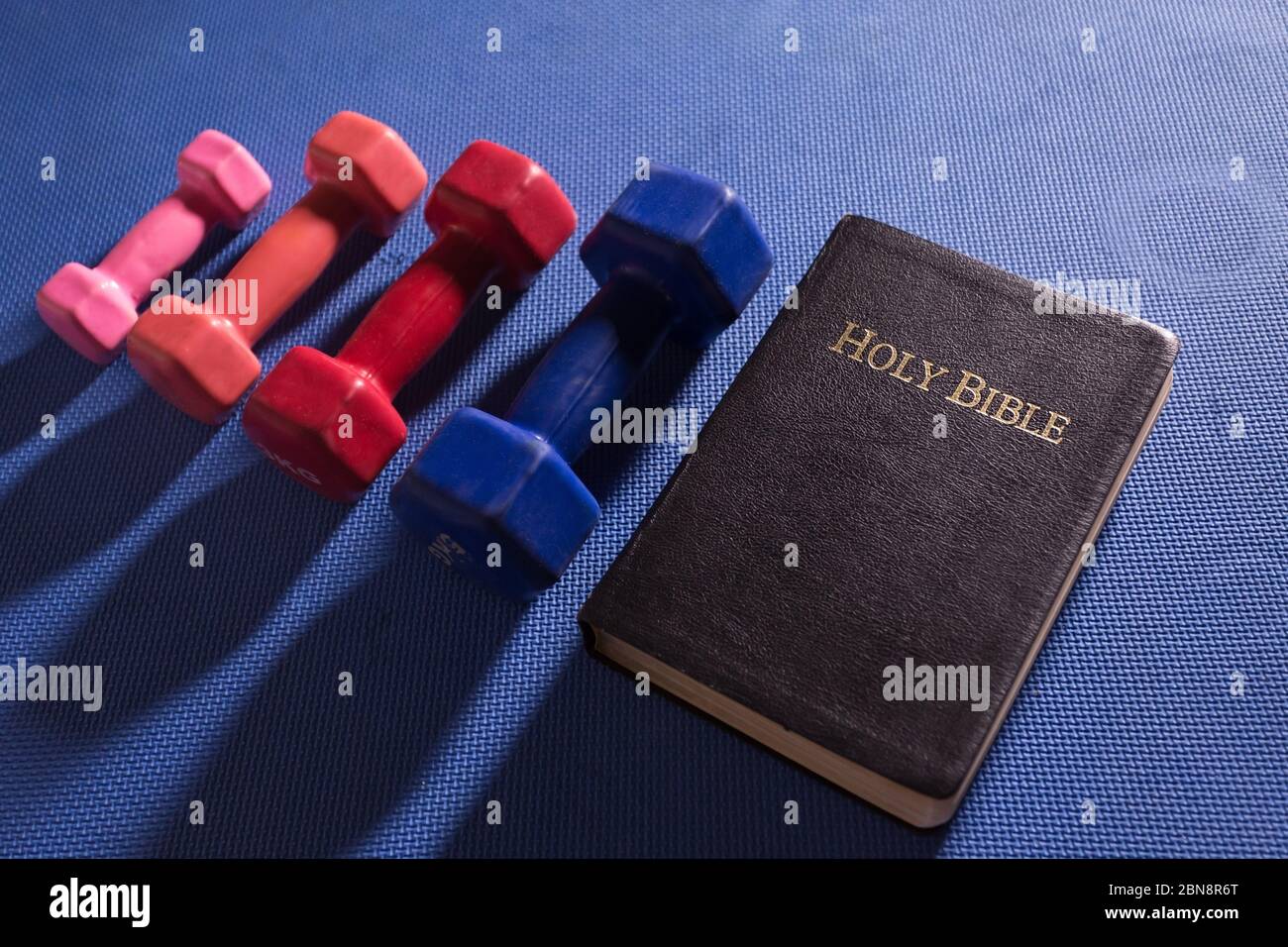 Dumbbells on a blue gym workout mat next to the Holy Scriptures Stock Photo