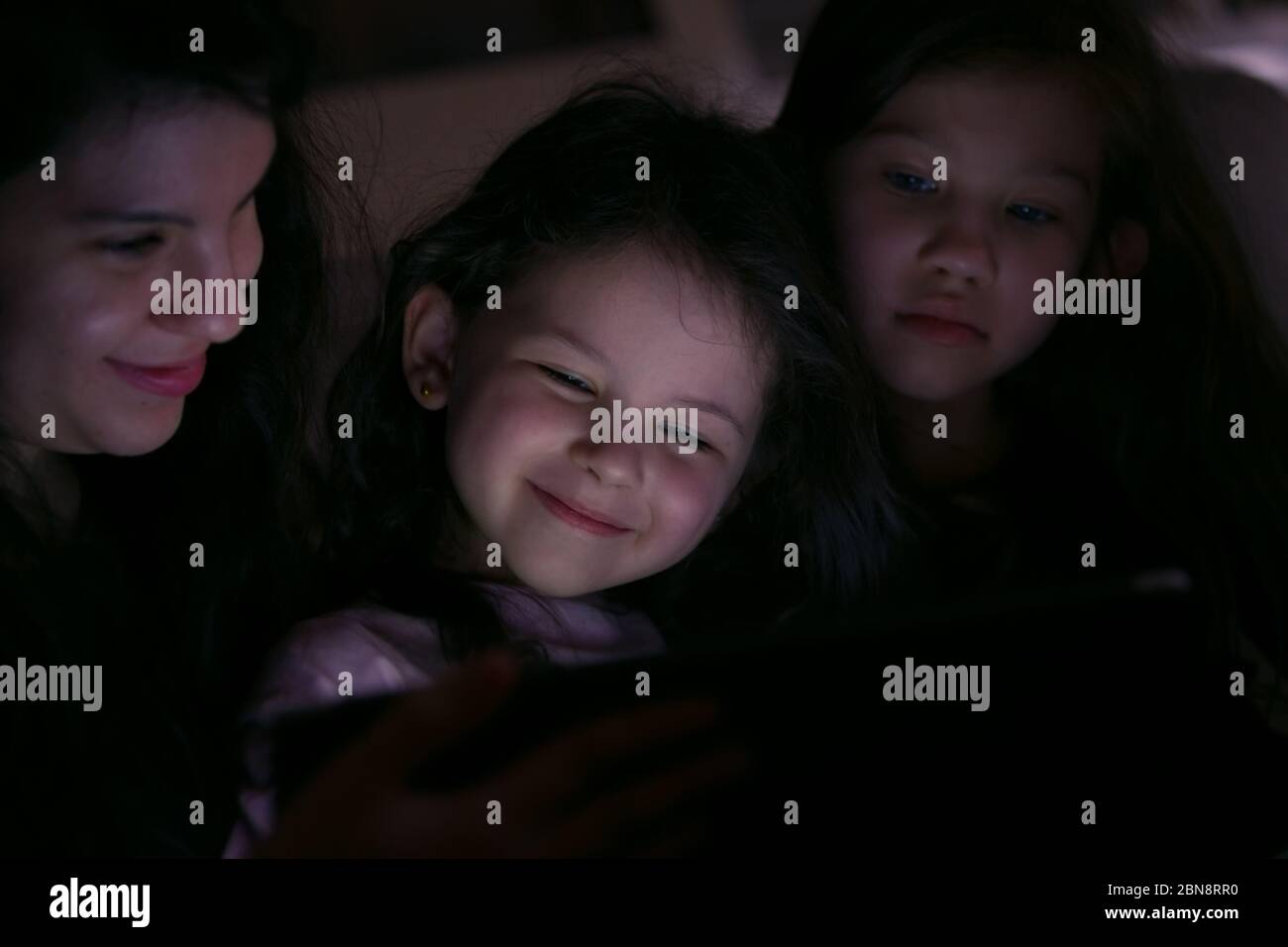 Young Mother watching a show with her children at home on in the dark Stock Photo