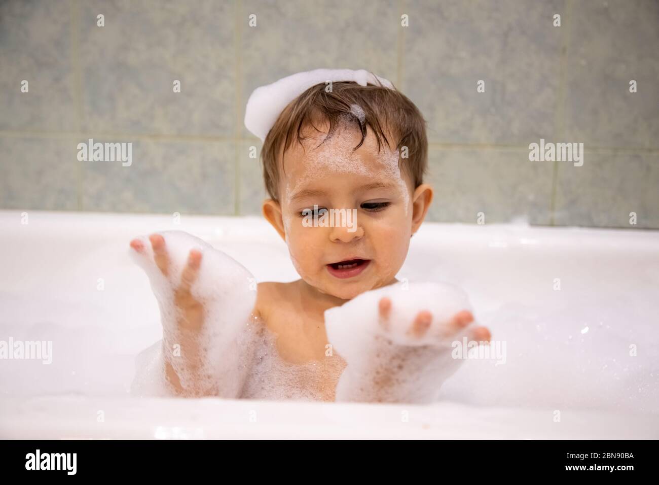 Cute baby boy taking a bath looking at soap foam in his hands. close up, soft focus, bacground