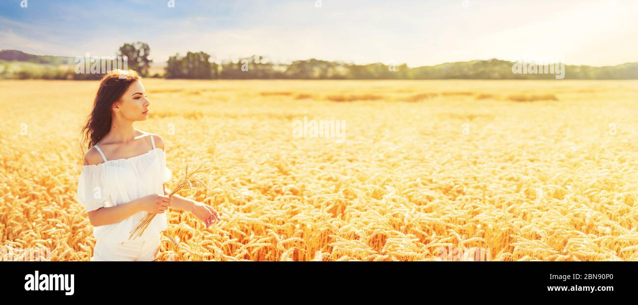 Beauty romantic girl enjoying nature in outdoors. Happy young woman in white shorts holding the ears on the field of golden ripe wheat in sun light. F Stock Photo