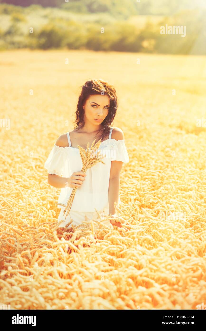 Beauty romantic girl enjoying nature in outdoors. Happy young woman in white shorts holding the ears on the field of golden ripe wheat in sun light. F Stock Photo