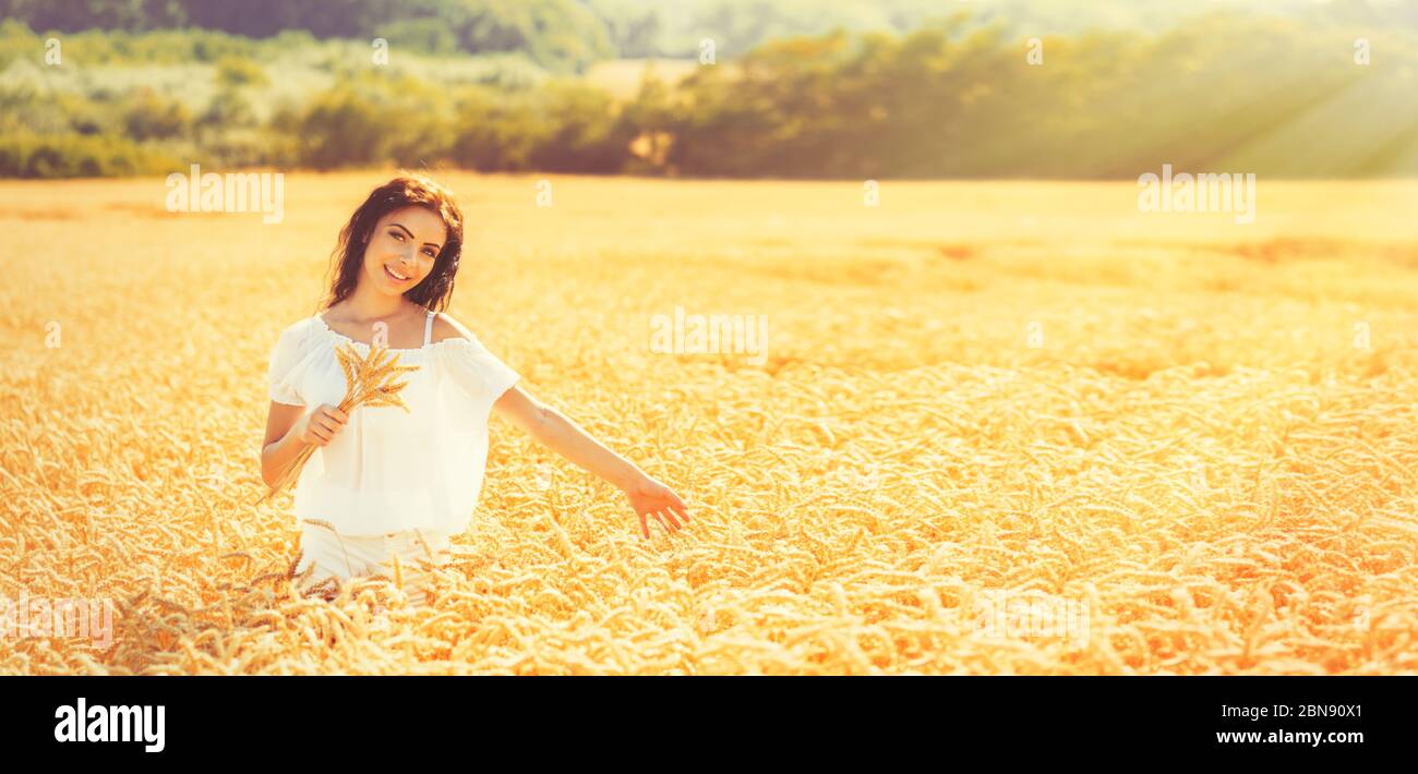 Beauty romantic girl enjoying nature in outdoors. Happy young woman in white shorts holding the ears on the field of golden ripe wheat in sun light. F Stock Photo