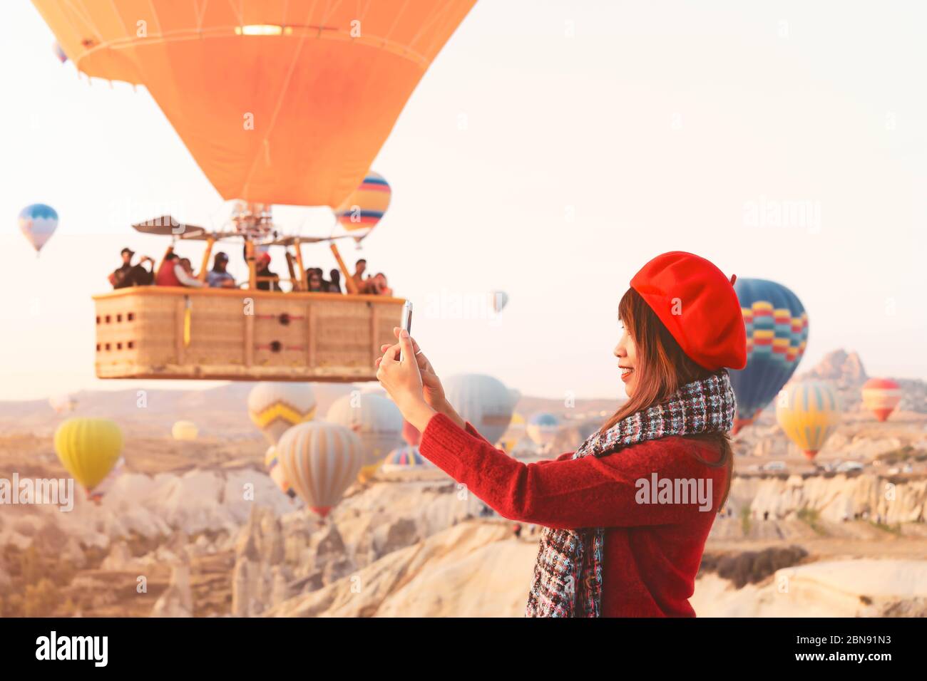Asain woman enjoy taking pictures of hot air balloons flying over amazing rock landscape in Cappadocia. Stock Photo