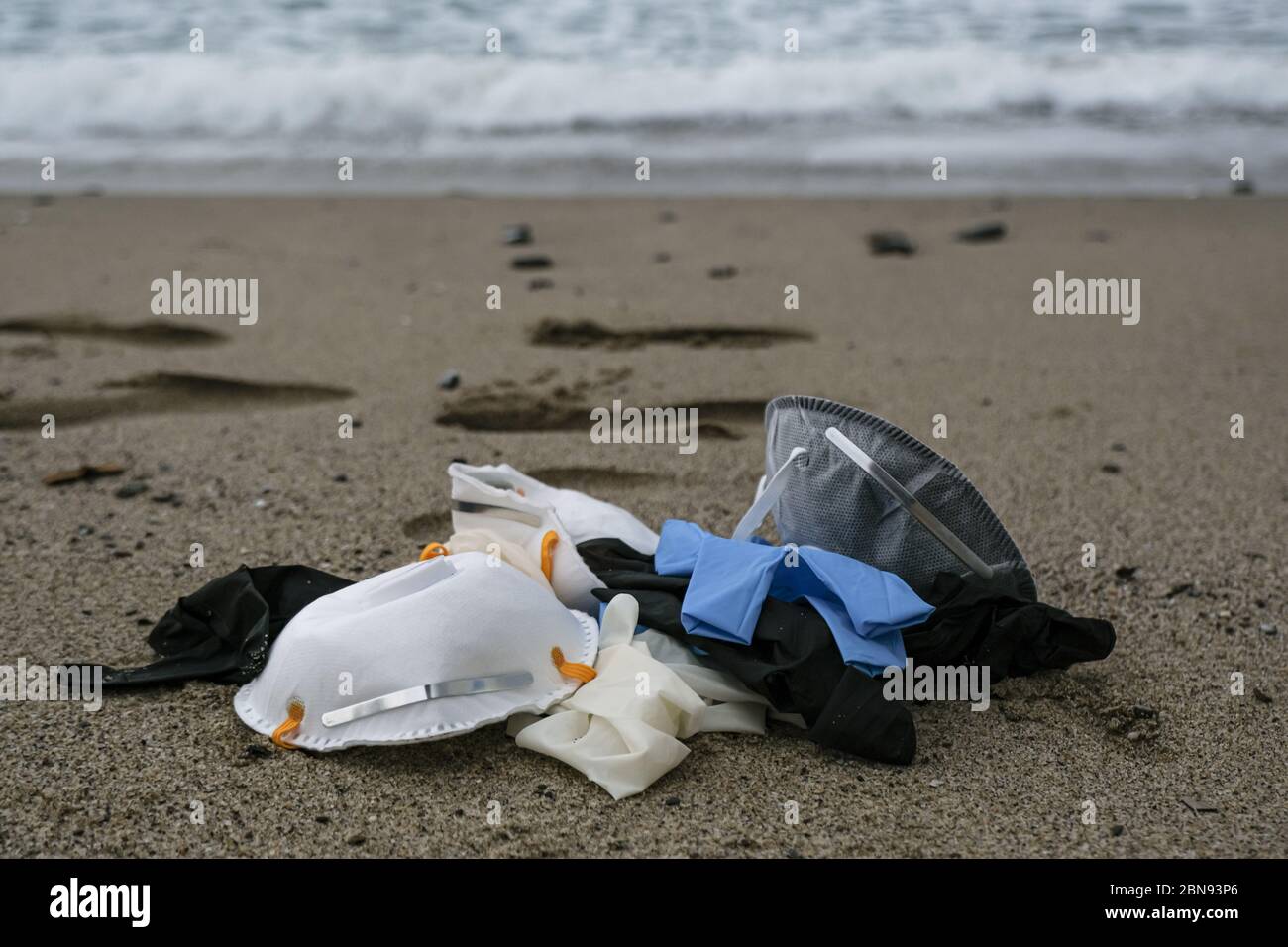 Protective virus mask and plastic gloves medical waste on sandy sea shore,coronavirus covid pollution disease  Stock Photo