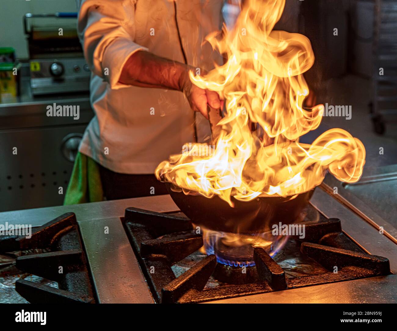 Chef Cooking With Fire In Frying Pan. Professional chef in a commercial