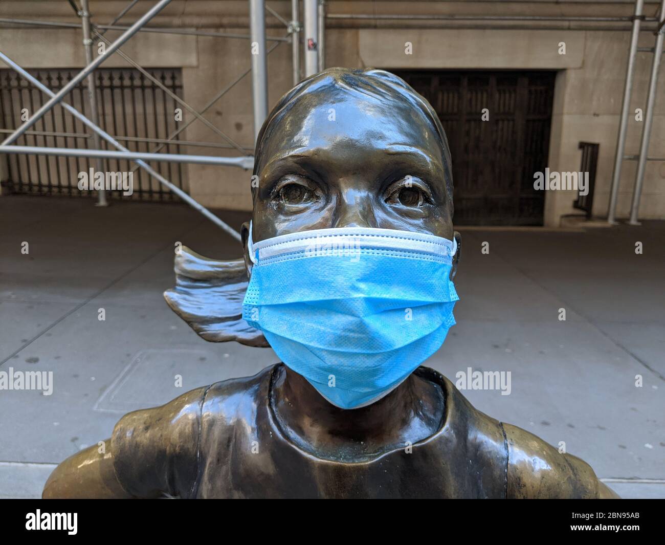 The Fearless Girl Statue with a mask during the coronavirus pandemic in New York City. Stock Photo