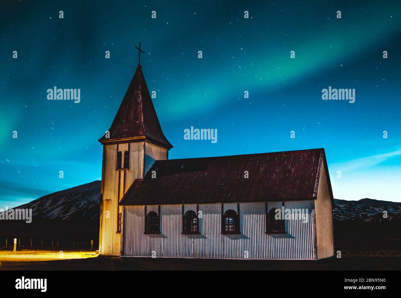 Beautiful green and blue Northern lights dancing over a little village church in Iceland. Stock Photo
