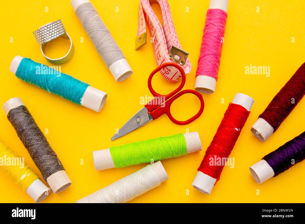 Thread, needles, scissors and meter on yellow background. tailoring set. sewing kit multi-colored Stock Photo
