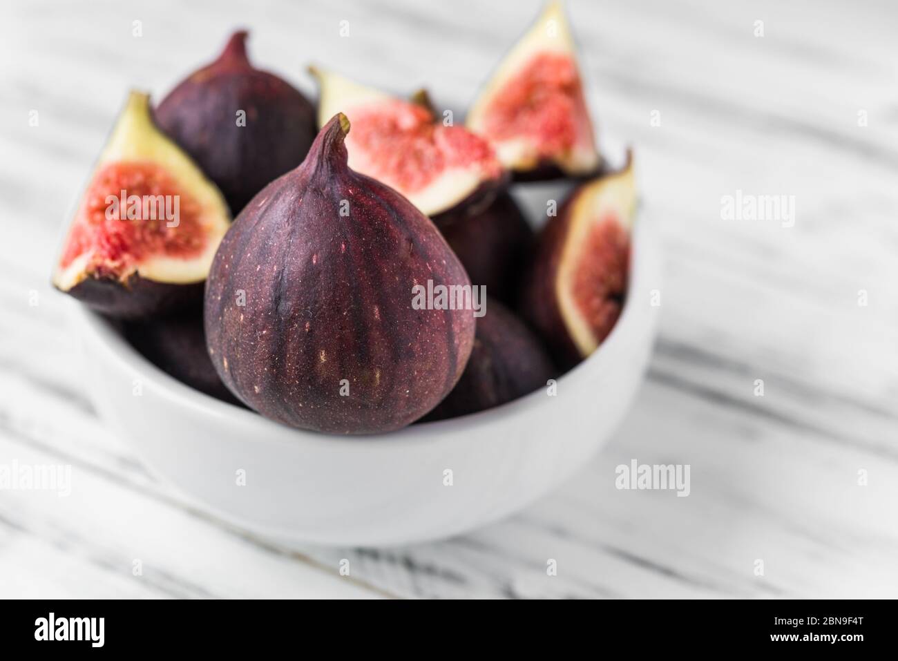 Close up of figs in a bowl against white wooden background. Stock Photo