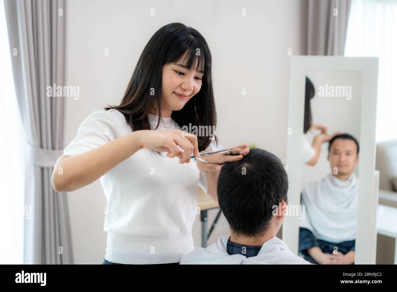 Asian young man with her girlfriend hairdresser cutting hair with Haircutting scissors at home they stay at home during time of home isolation against Stock Photo