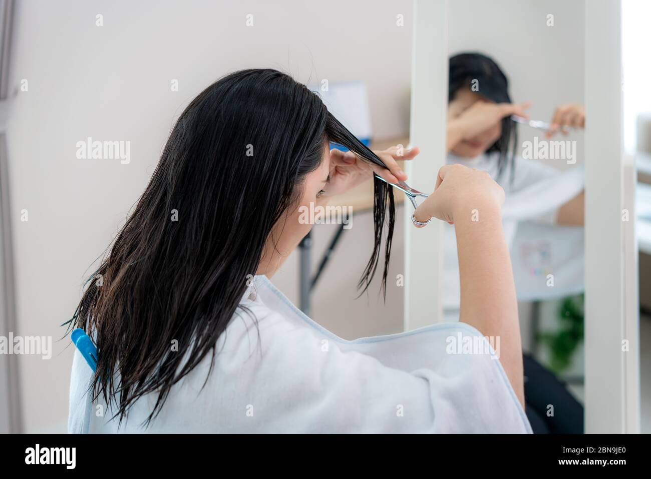 Asian woman cutting own her hair with haircutting scissors at home they stay at home and shelter In place during time of home isolation against Novel Stock Photo
