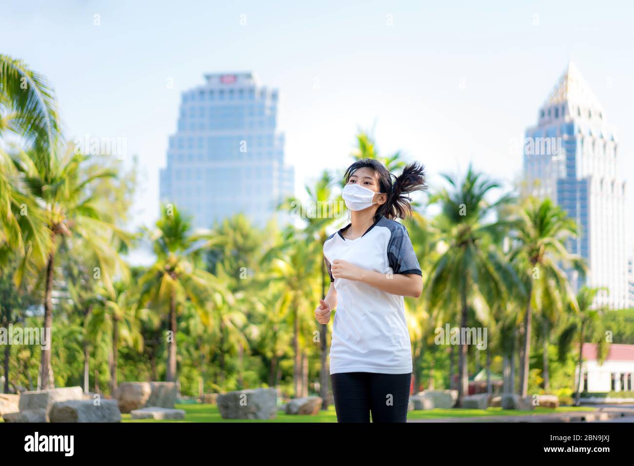 Asian young woman are jogging and exciseing outdoor in city park and wearing protective mask on face for stay in fit during Covid-19 pandemic in Bangk Stock Photo