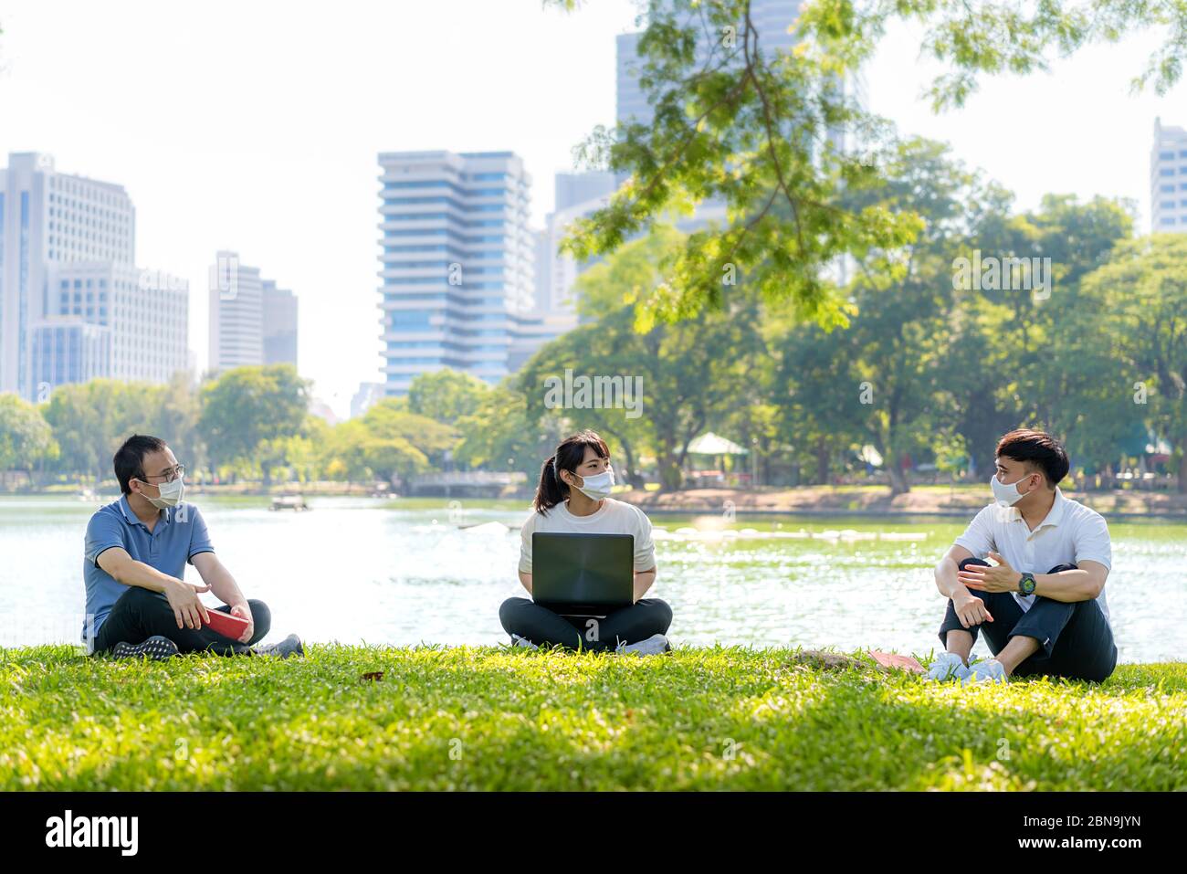 Asian young three man and woman talking and relaxing with they friend and wearing mask sitting distance of 6 feet distance protect from COVID-19 virus Stock Photo