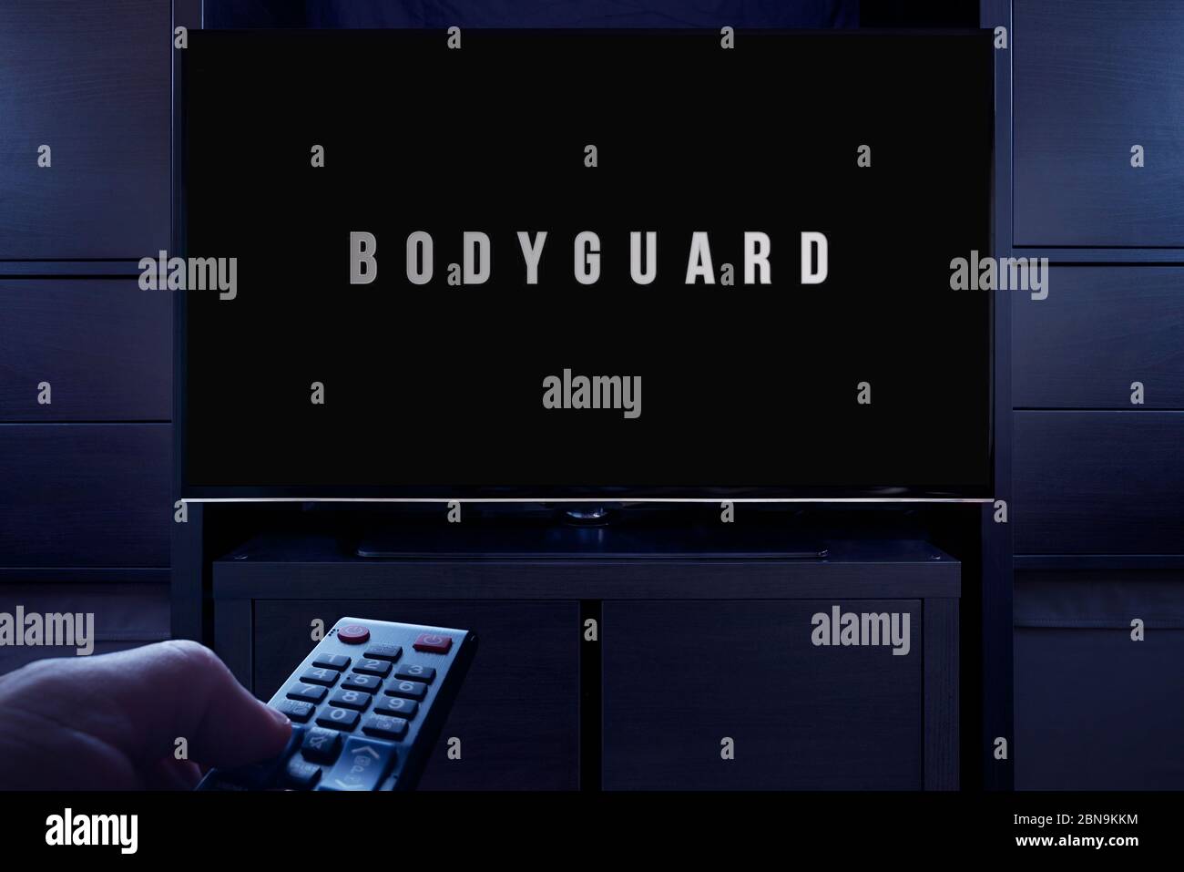 A man points a TV remote at the television which displays the Bodyguard main title screen (Editorial use only). Stock Photo