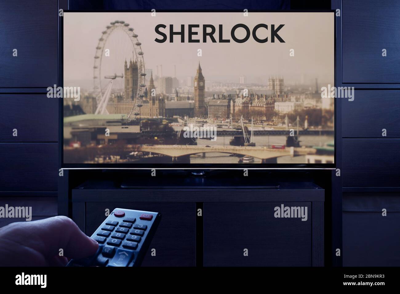 A man points a TV remote at the television which displays the Sherlock main title screen (Editorial use only). Stock Photo