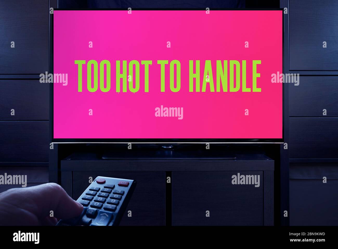 A man points a TV remote at the television which displays the Too Hot To Handle main title screen (Editorial use only). Stock Photo