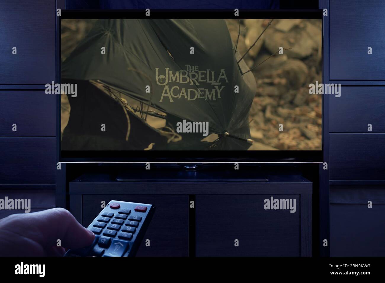 A man points a TV remote at the television which displays the The Umbrella Academy main title screen (Editorial use only). Stock Photo