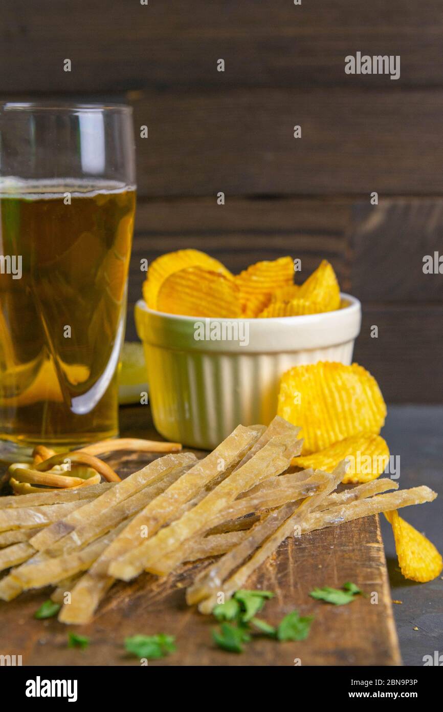 Dried salted tuna elite snack with beer, lemon and potato chips on dark wooden board. Snack on fish with beer. Front views, close-up Stock Photo