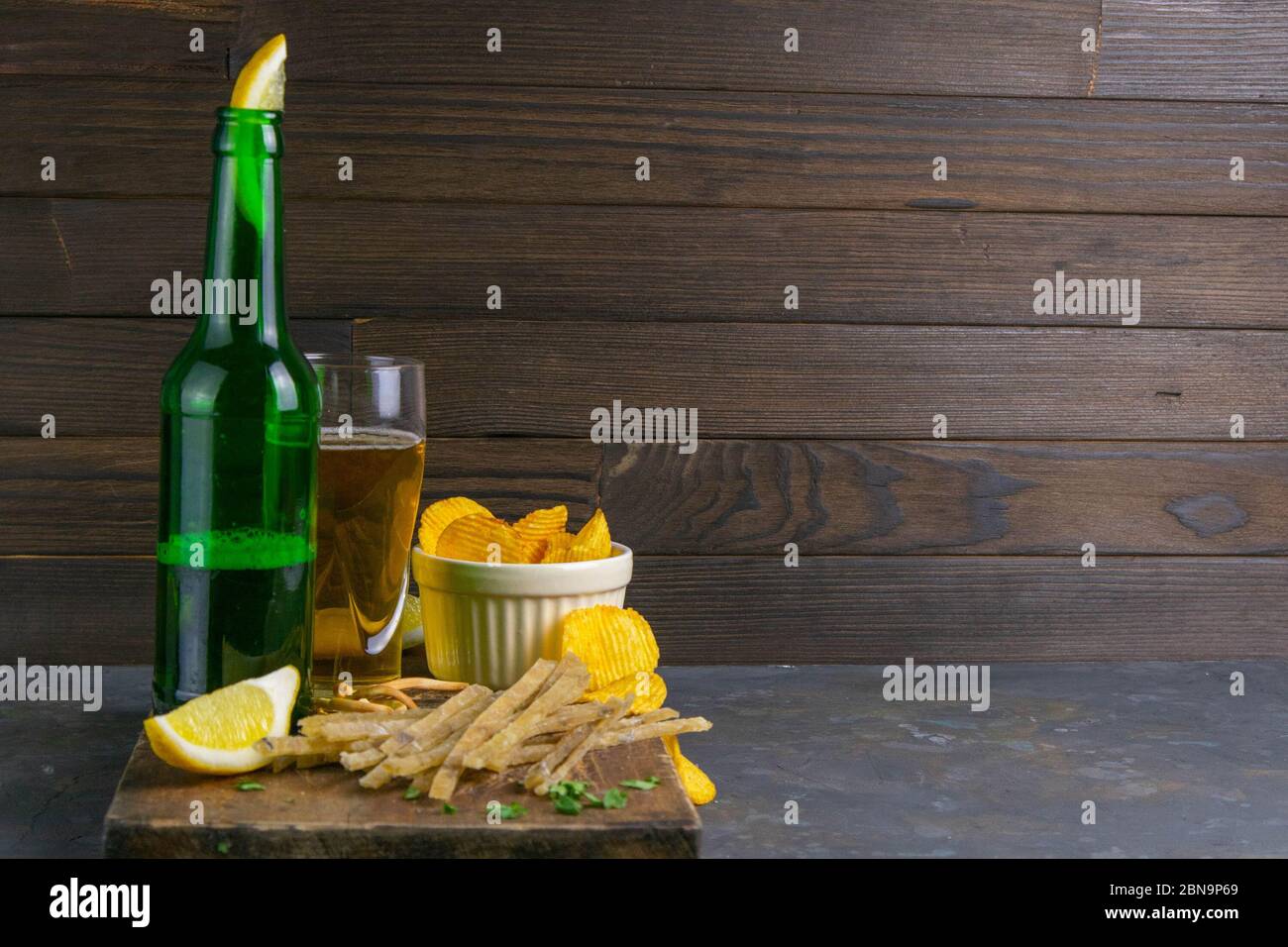 Dried salted tuna meat strips with beer, lemon and potato chips on dark wooden board. Snack on fish with beer. Front views with clear space Stock Photo