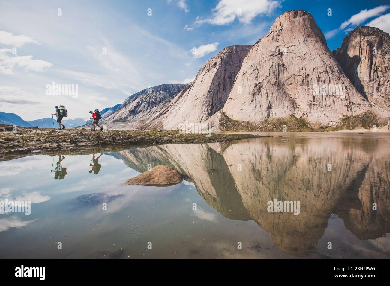Reflection of two backpackers hiking below steep mountains Stock Photo