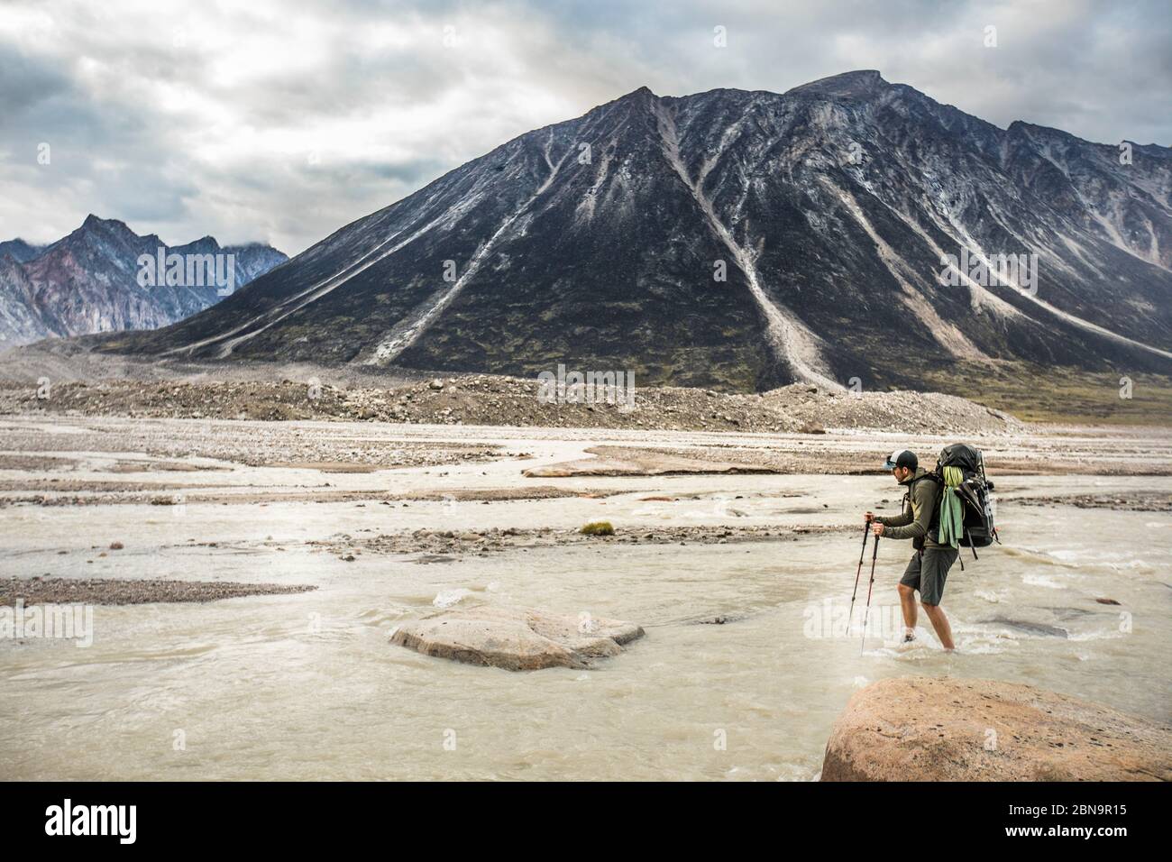 Hiker faces adversity, crossing a braided river channel. Stock Photo