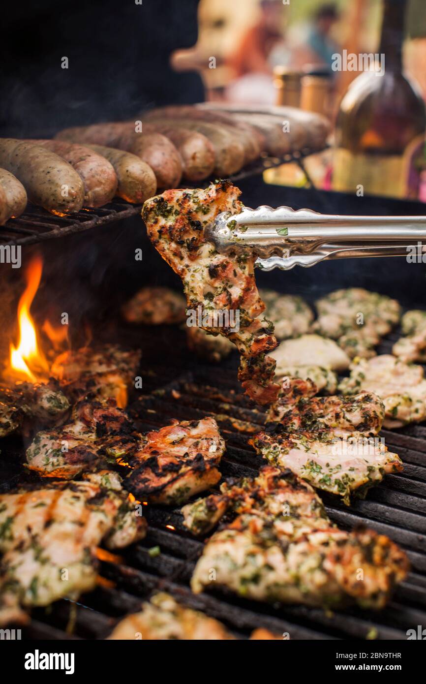 Grill full of marinated chicken and brats with open flame Stock Photo